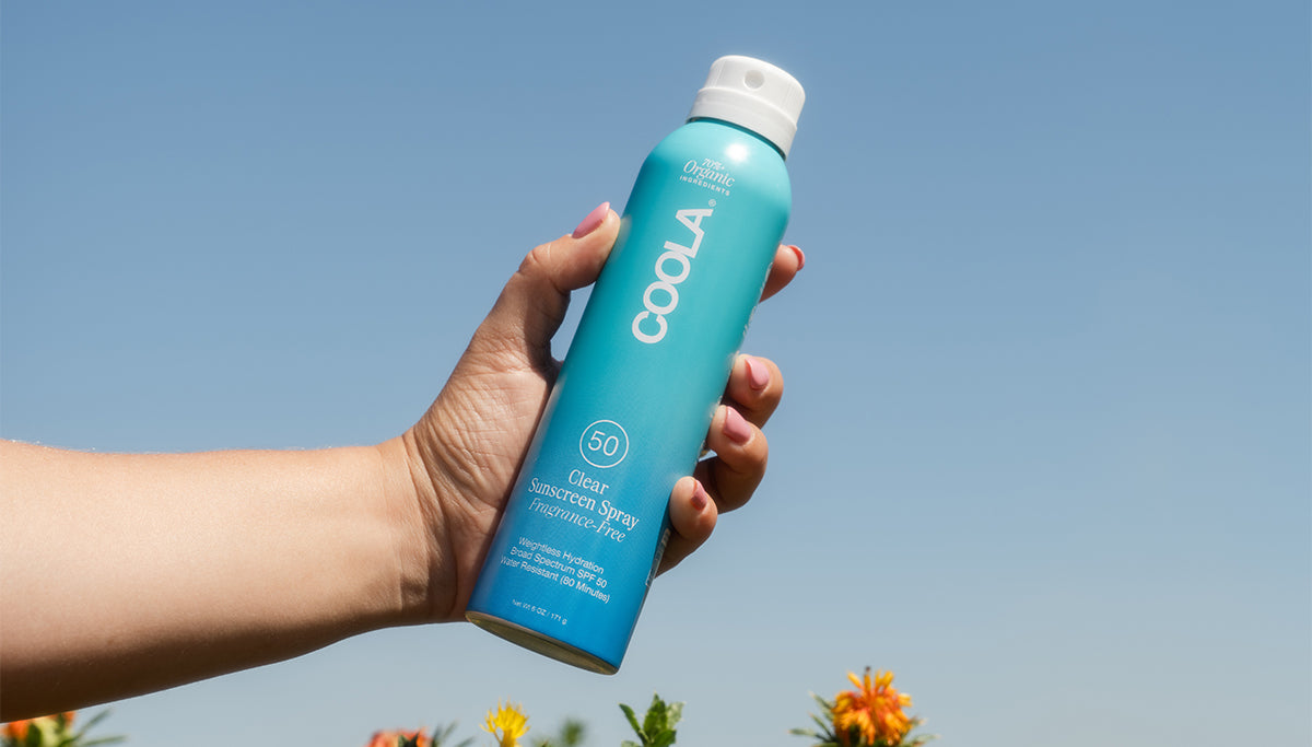 Hand holding COOLA's Clear Sunscreen Spray 