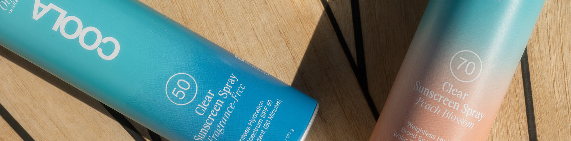 COOLA SPF 50 and SPF 70 Clear Sunscreen Sprays on Wood.